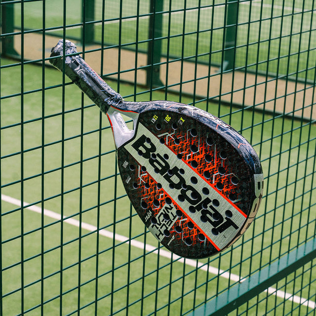 Tennis racket with Babolat branding against a green fence on a tennis court
